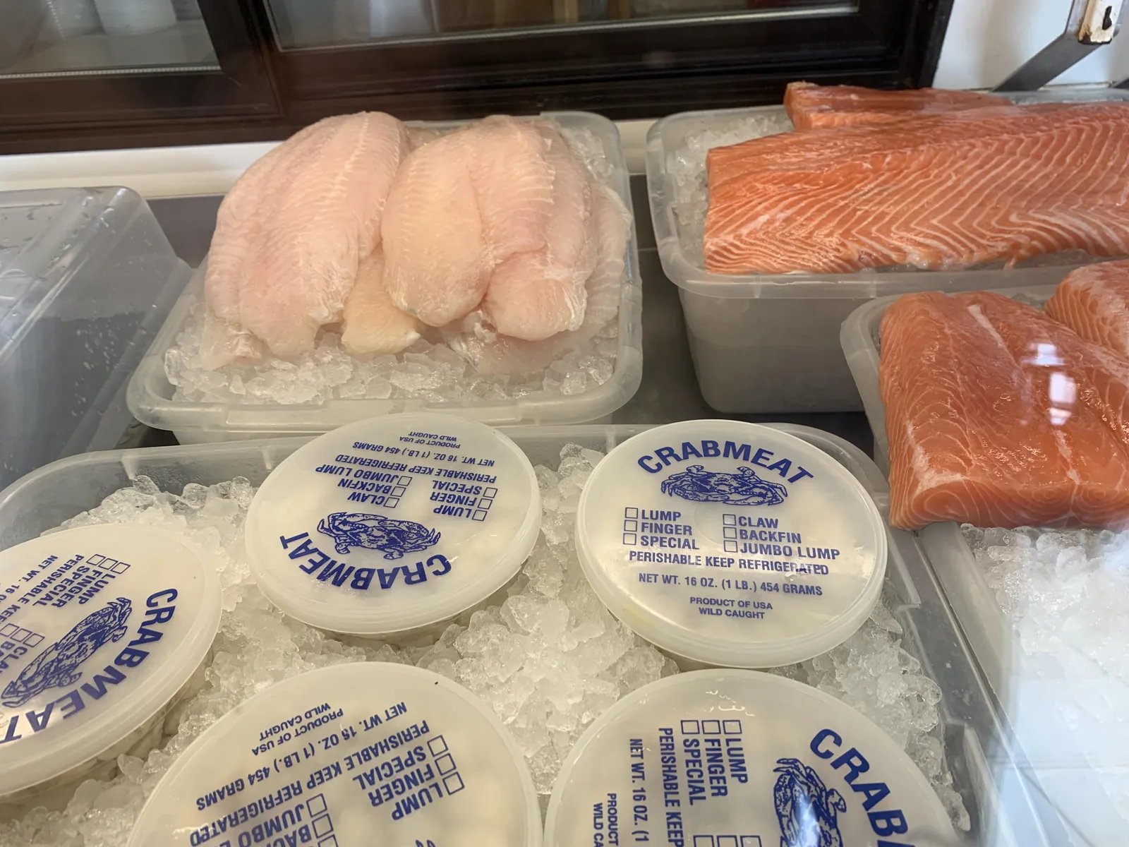 Fresh jumbo lump crab meat tubs and fish fillets on ice at Fountain View Fish Market in Houston